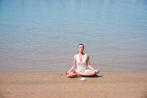 girl meditating in yoga pose with coffee cup at water