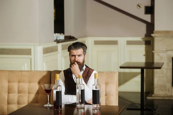 Hipster sentado en el sofá con vaso de martini y tres botellas — Foto de Stock