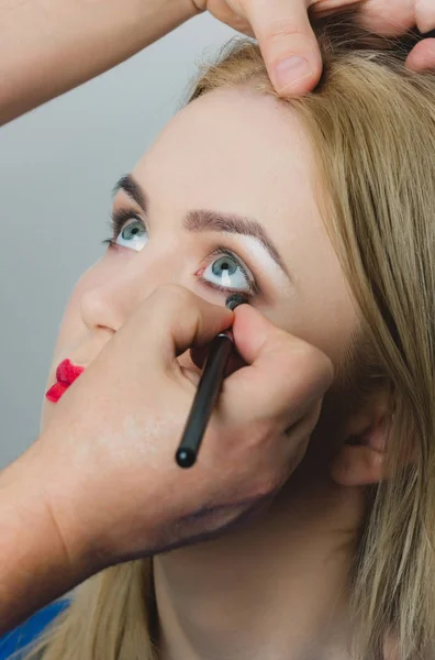 Maquillaje artista aplicando delineador de ojos en la cara chica — Foto de Stock