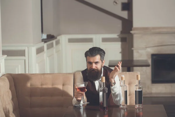 Człowiek siedzi na kanapie z martini szkła i trzy butelki — Zdjęcie stockowe