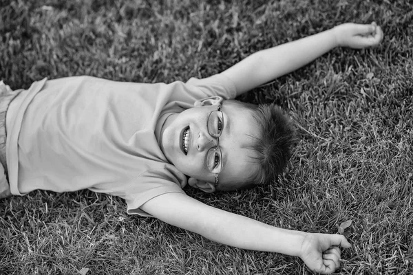 Menino feliz com cabelo em óculos na grama — Fotografia de Stock