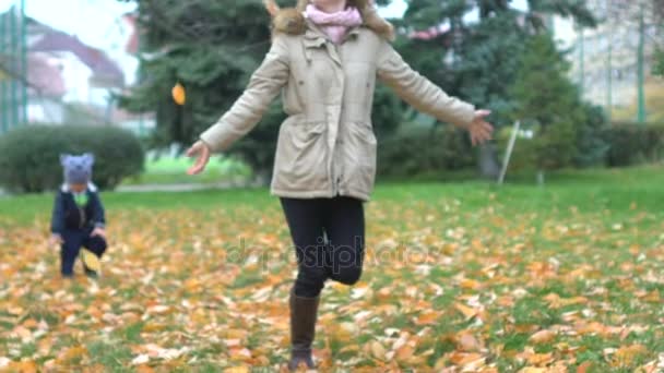 Mamá, hijo jugando a las hojas de otoño en el parque del jardín. Caminar sobre la naturaleza de otoño, juegos al aire libre, correr a lo largo de la hierba y tirar hoja de oro amarillo. Entretenimiento en noviembre. Infancia y maternidad, felicidad familiar — Vídeos de Stock