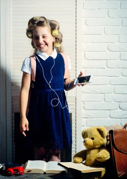 Menina pequena com curler no cabelo com fone de ouvido e telefone . — Fotografia de Stock