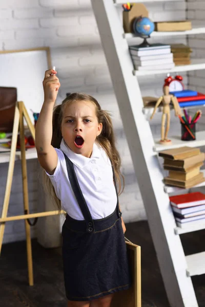 Menina com cara irritada perto de material escolar e estante — Fotografia de Stock