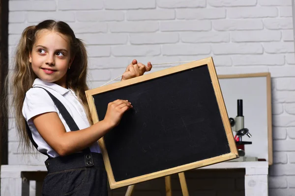 Schoolgirl with cunning face holds small blackboard — Stock Photo, Image