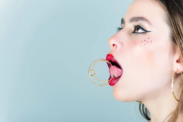 Kvinna med fashionabla makeup hålla smycken örhänge på tungan — Stockfoto