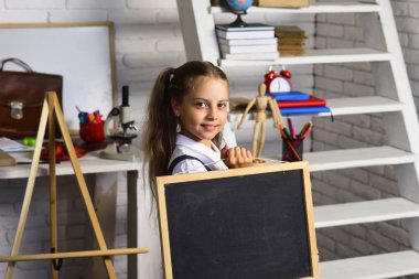 Kız öğrenci kara tahta hafif tuğla duvar sınıf arka plan üzerinde tutar.