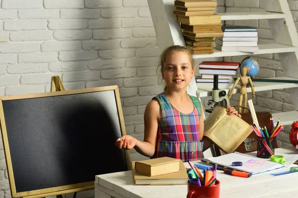 Школярка з усміхненим обличчям тримає відкриті книги. Дівчина біля крейдяної дошки — стокове фото