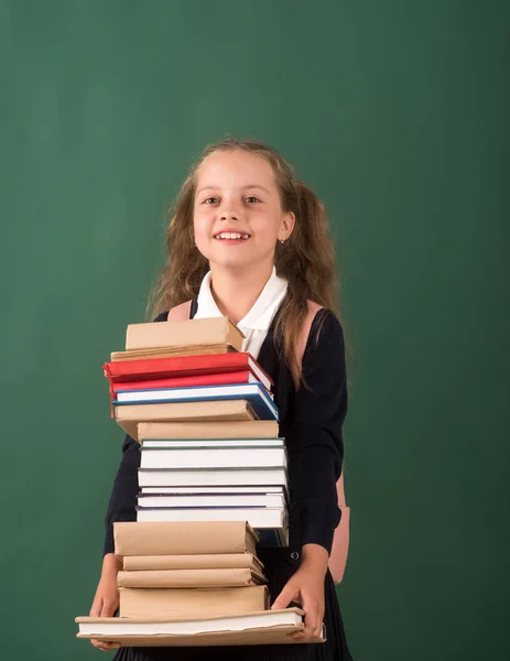 Школьница с улыбкой на лице держит огромную кучу книг — стоковое фото