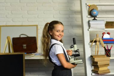 Çocuk deneyler yapar. Kız öğrenci mikroskop hafif sınıf arka plan üzerinde tutar.