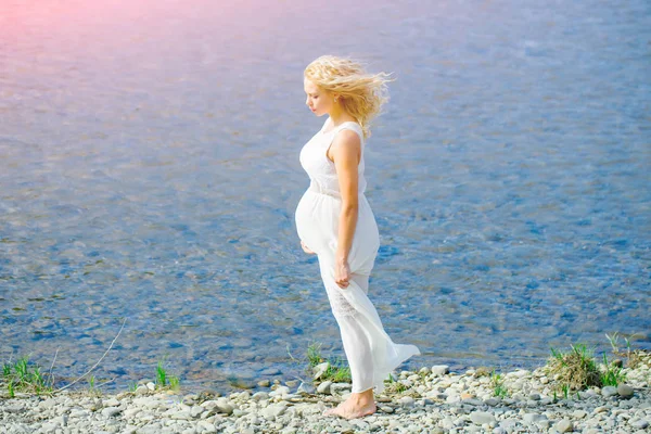 Zwangere vrouw in witte jurk wandelen aan zee strand — Stockfoto