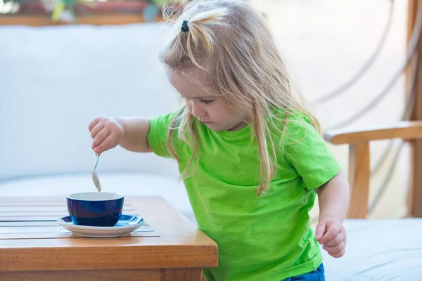 Niño con el pelo largo rubio mezclando azúcar con cucharadita . — Foto de Stock