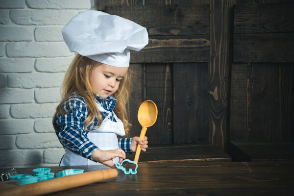 Child using spoon, rolling pin and cutters on table