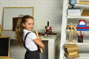 Kız öğrenci ders kitabı hafif tuğla duvar sınıf arka plan üzerinde tutar.