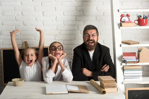 Meninas e homem barbudo sentam-se na mesa com livros — Fotografia de Stock