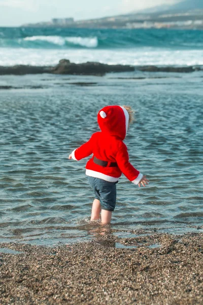 Süßer kleiner Junge in rotem Weihnachtsmannmantel im Meerwasser — Stockfoto