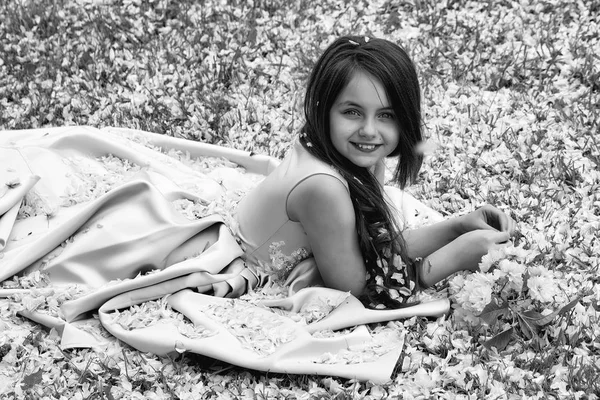 Little girl on green grass with petals — Stock Photo, Image