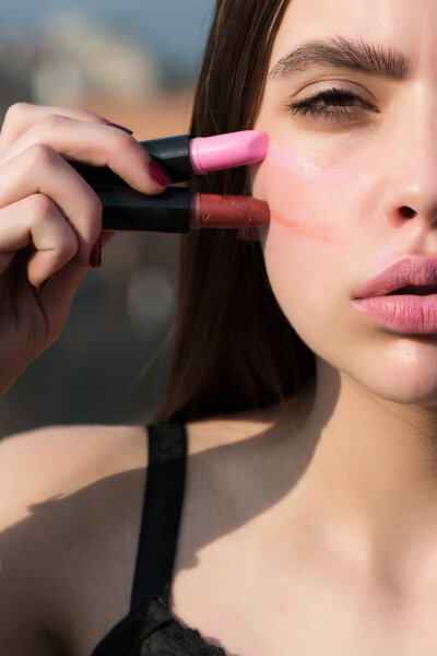 Девушка позирует с двумя помадами и половинкой лица
