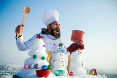 Mavi gökyüzü üzerinde heyecanlı aşçı, kardan adam ve kar xmas ağacı