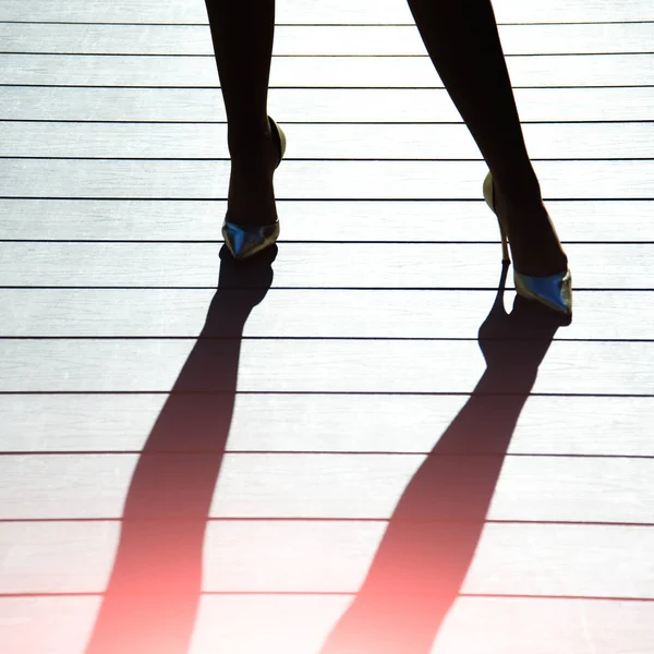 Patas femeninas en zapatos dorados con tacones altos y sombra — Foto de Stock