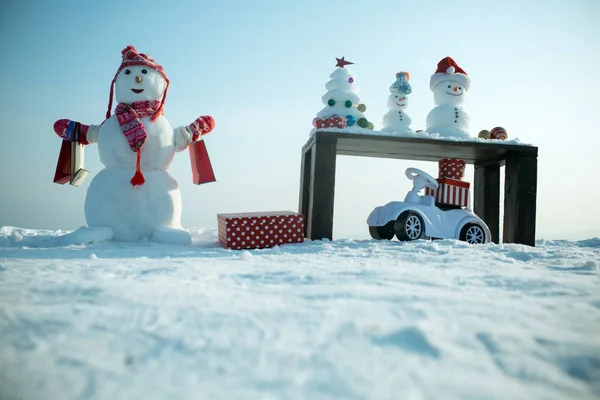Sneeuwpop met boodschappentassen op besneeuwde achtergrond — Stockfoto