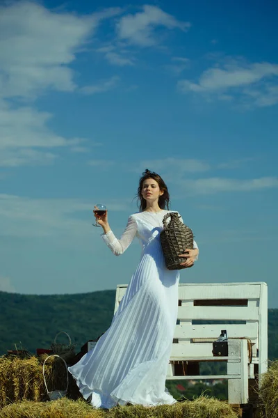 Mujer con copa de vino tinto y botella de mimbre — Foto de Stock