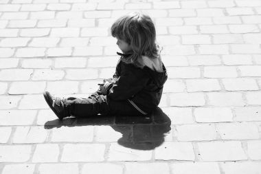 Kaldırım taşları üzerinde küçük bir çocuk oturur