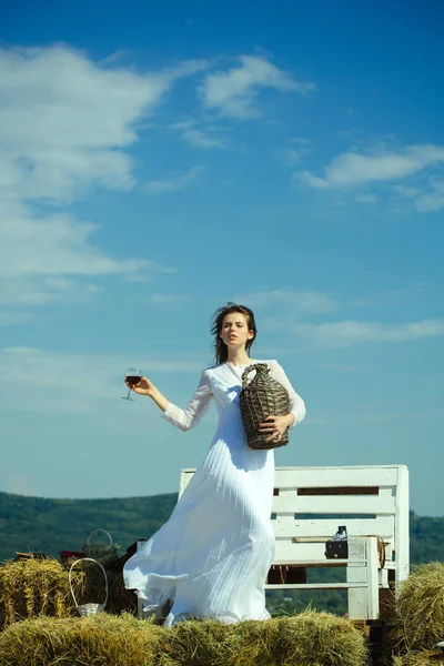 Mulher com copo de vinho tinto e garrafa de vime — Fotografia de Stock