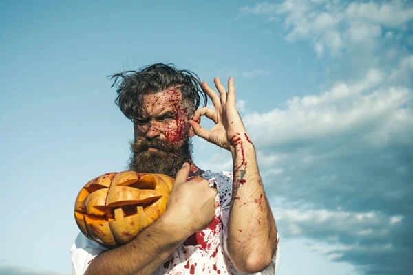 Halloween uomo tenendo zucca sanguinosa sul cielo nuvoloso blu — Foto Stock