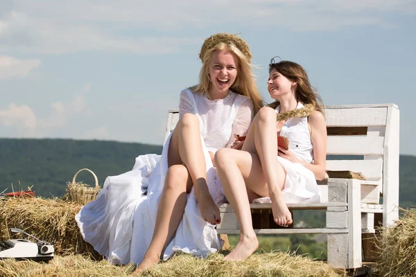 Twee meisjes zitten op bankje op hooi — Stockfoto