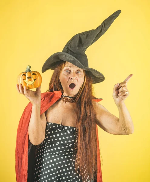 Halloween señora mayor con la calabaza señalando el dedo sobre fondo amarillo — Foto de Stock