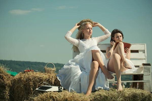 Twee meisjes zitten op bankje op hooi. — Stockfoto