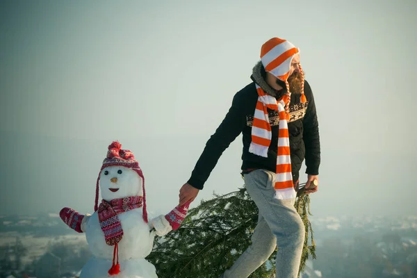 Hipster trascinando albero di Natale sul paesaggio invernale innevato — Foto Stock