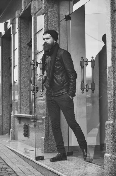 serious bearded man hipster exit glass door in leather jacket