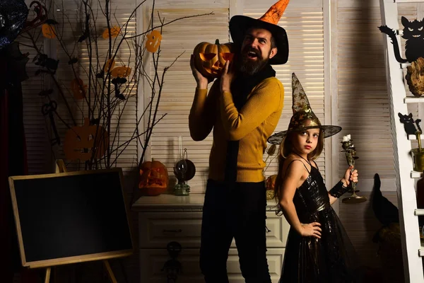 Wizard and little witch in hats hold candlestick and pumpkin