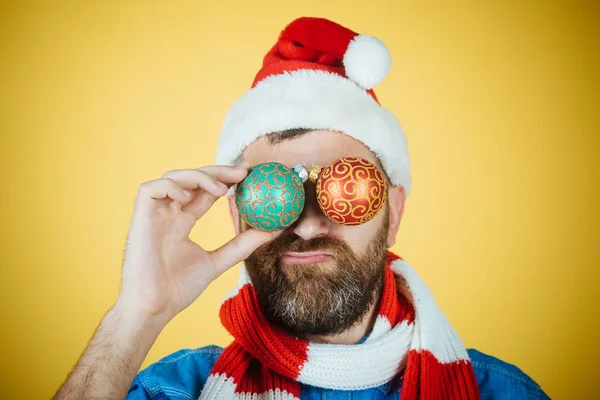 Natal homem cobrir os olhos com bolas de xmas no fundo amarelo — Fotografia de Stock