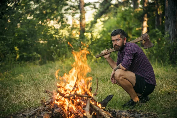 Hipster homme avec hache regarder la flamme du feu de camp — Photo