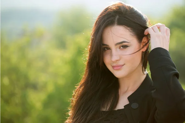 Woman touch long brunette hair on natural landscape