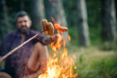 Doğal zemin üzerine bulanık adamla ateşin ortasına sosis kavrulmuş