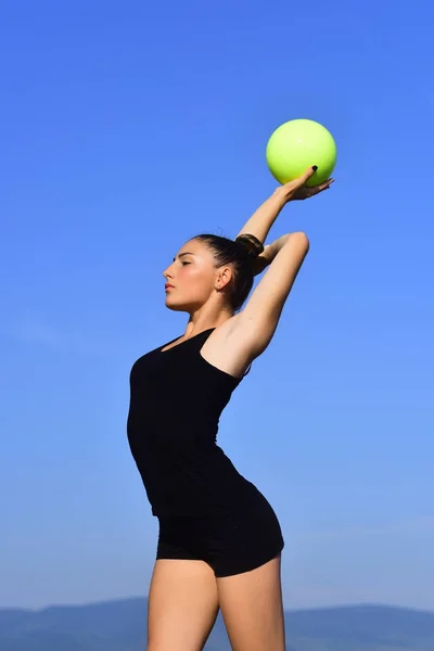 Mujer gimnasta en ropa deportiva negra con bola verde . — Foto de Stock