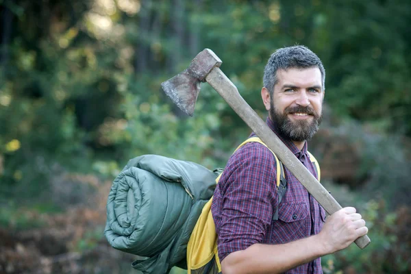 Hipster leñador con barba y sonrisa celebrar mochila y hacha —  Fotos de Stock