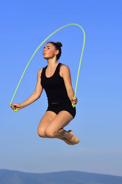 Woman gymnast in black sportswear with green jump rope