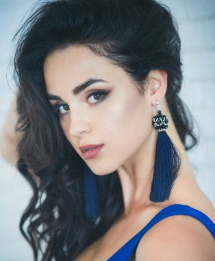 Yüz makyaj, mavi küpe püsküllü, uzun esmer saçlı kızla