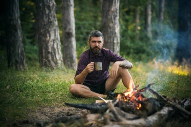 Hipster hiker kupa ile rahatla ormandaki şenlik ateşi