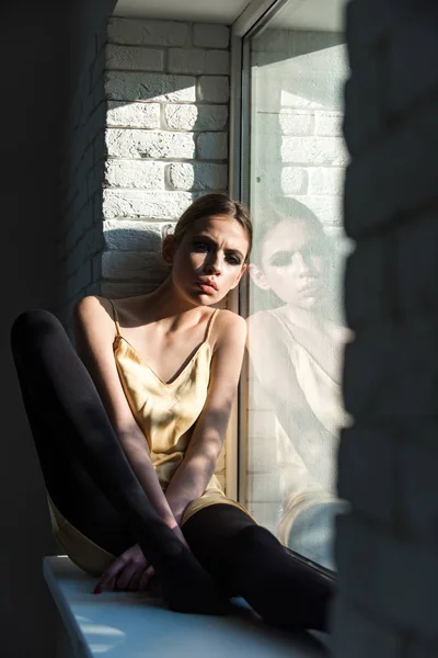 Žena s tváří myšlení sedět sám na okenní parapet v interiéru — Stock fotografie