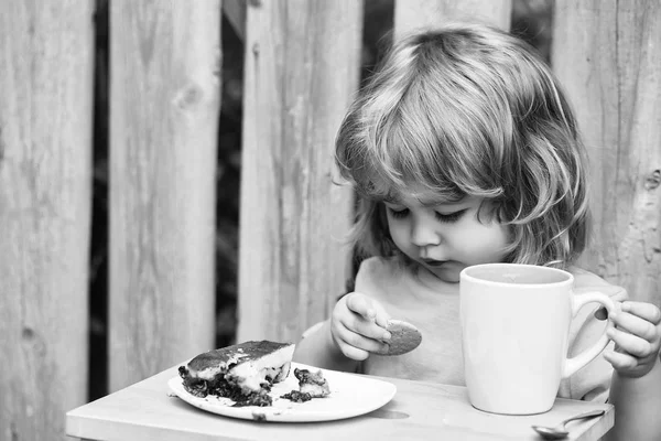 Piccolo ragazzo mangiare torta vicino recinto di legno — Foto Stock