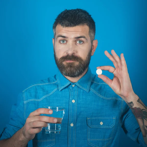 Muž s vousy hold vodního skla na modrém pozadí, bolest hlavy. — Stock fotografie