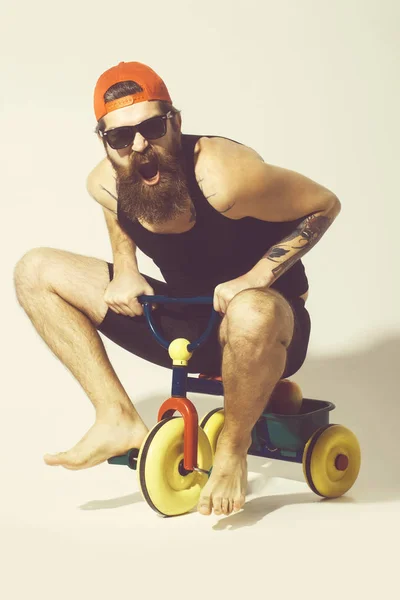 Barbudo gritando homem no colorido bicicleta brinquedo em óculos de sol, cap — Fotografia de Stock