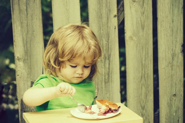 Kleine jongen eten taart in de buurt van houten hek — Stockfoto