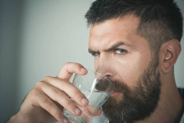 Mies, jolla on parta vakavissa kasvoissa juo vettä lasista — kuvapankkivalokuva
